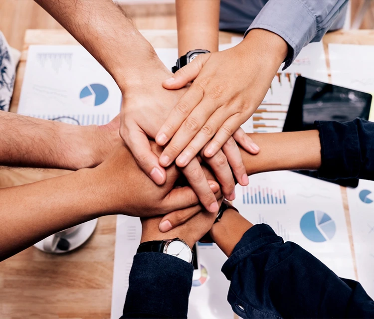 About Us 7 A diverse group of hands stacked together over business charts, symbolizing teamwork, collaboration, and unity among skilled professionals.